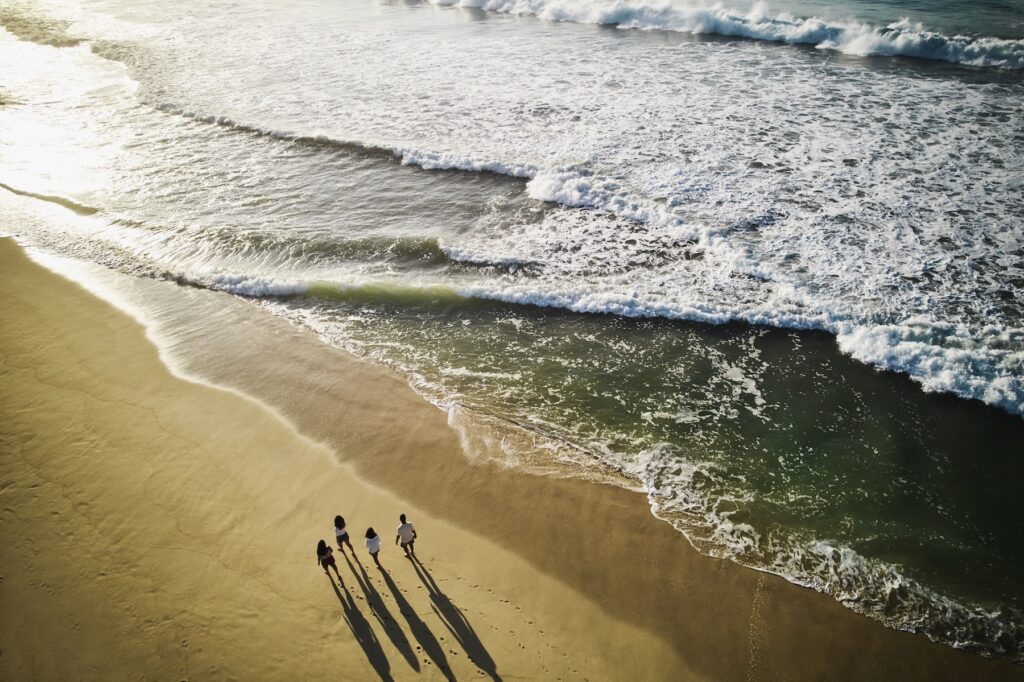Flygbild av strand med en familj som promenerar på den i vattenbrynet.