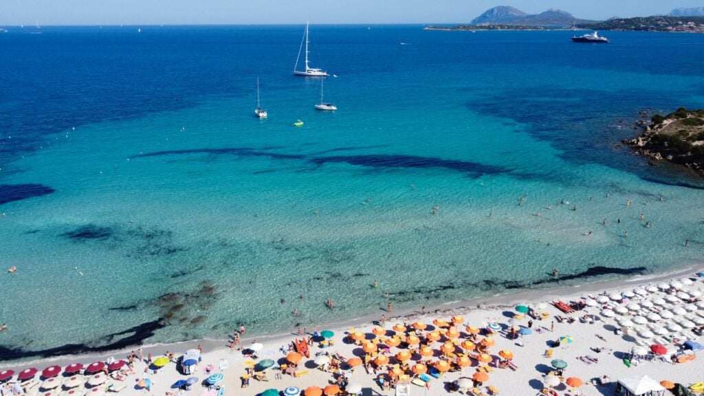 Flygbild av strand på Sardinien med många solstolar.