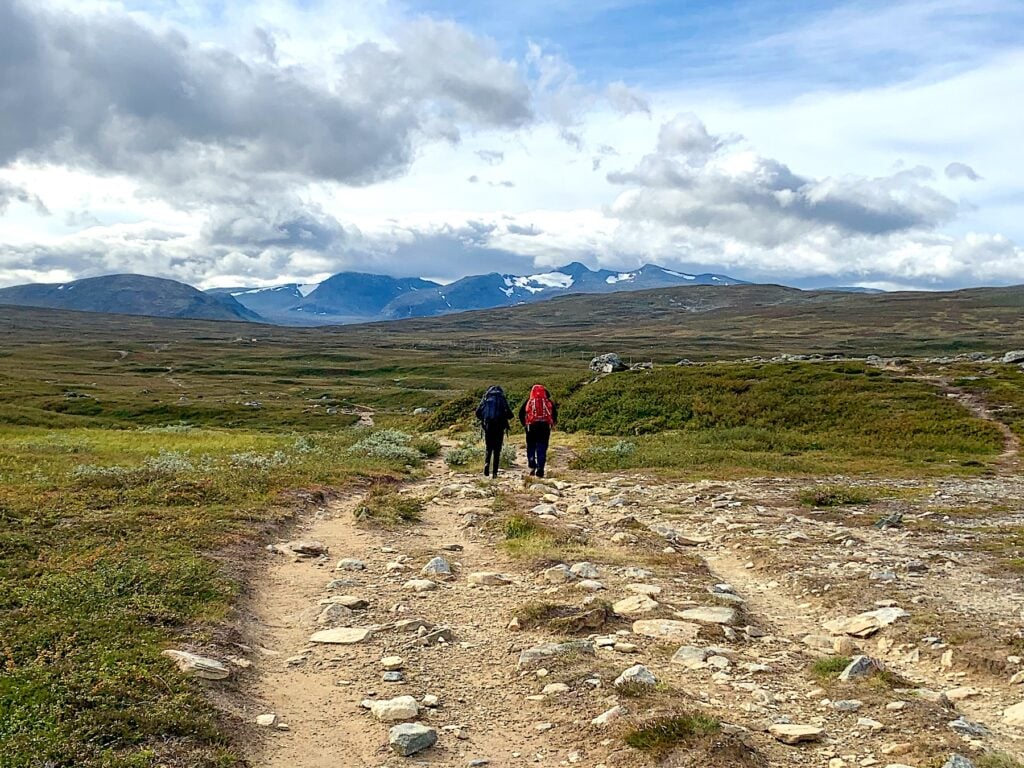 Två fjällvandrare med ryggsöäckar på stenig stig i fjällen.