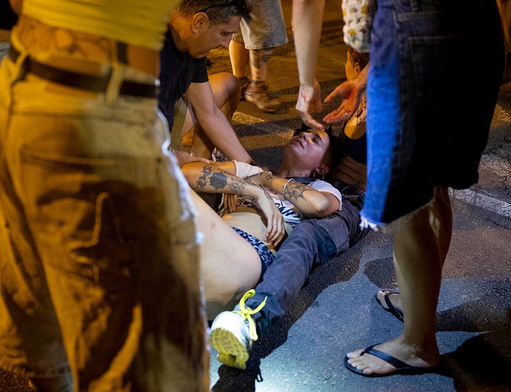 Skadad kvinna ligger på marken omringad av människor.