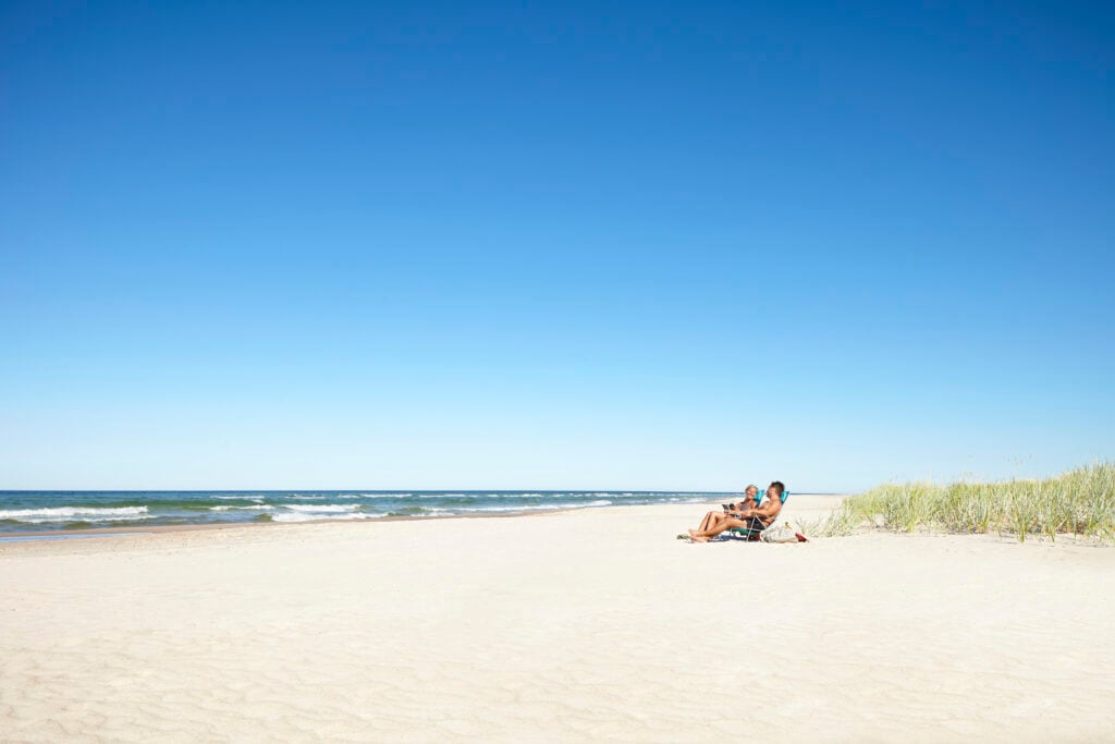 Ett par sitter på en kritvit strand bredvid havet under en klarblå himmel.