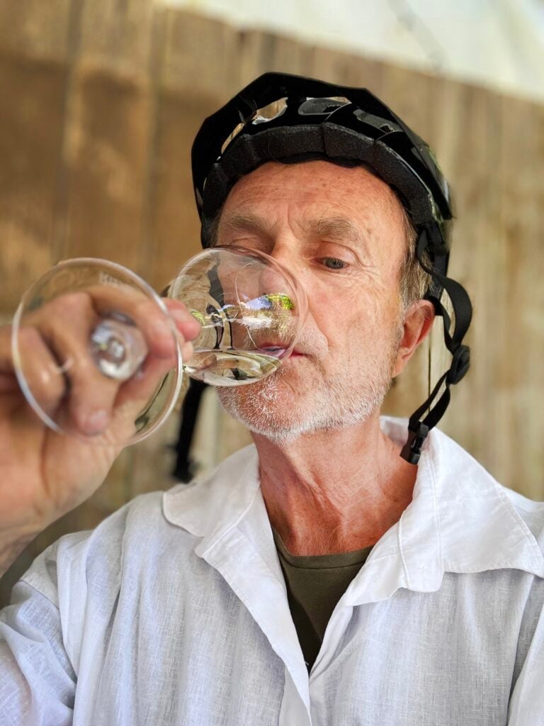 Man med vit skjorta och cykelhjälm som dricker vin.