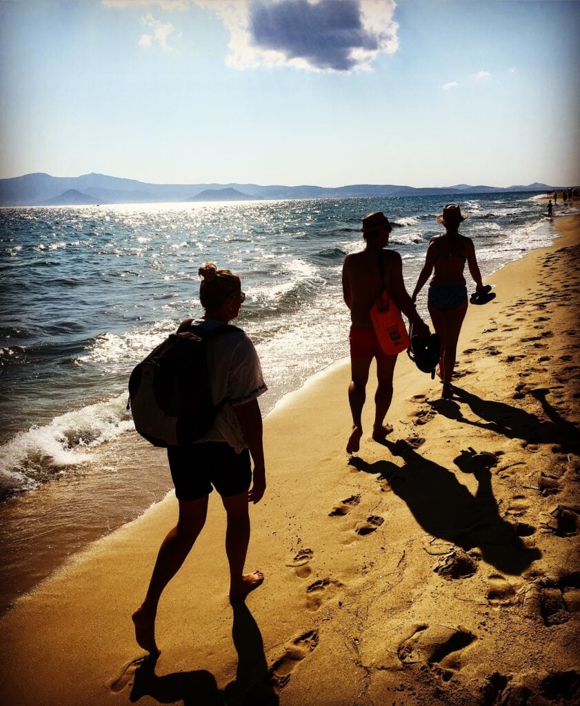 Tre turister som vandrar på en sandstrand.