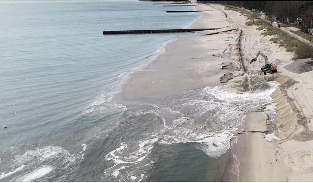 Sandstrand med grävskopa som gräver i sanden.