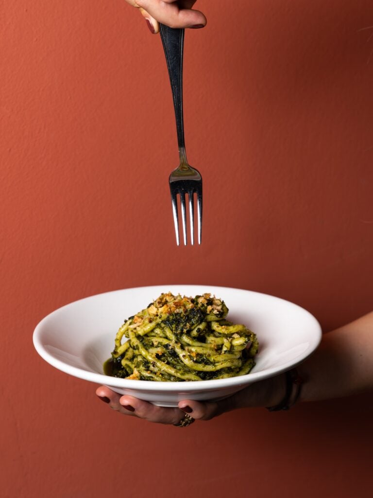 Tallrik med pasta och en gaffel som hänger ovanför.