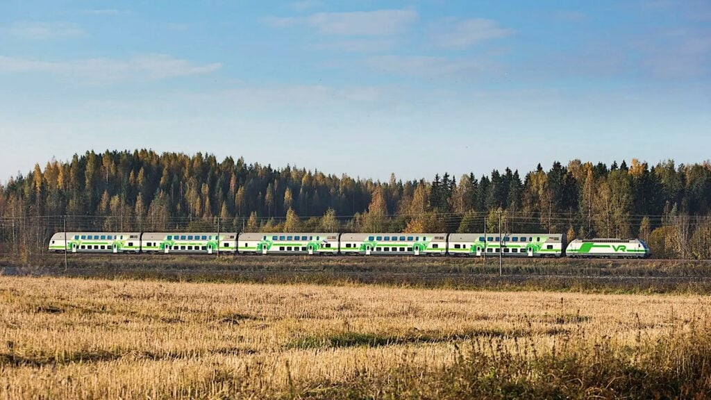 Tåg med gröna färger som kör i höstlandskap.
