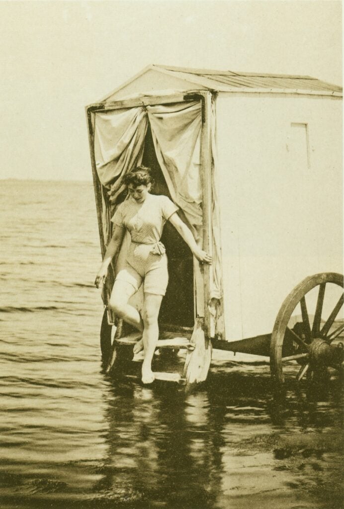 Kvinna i baddräkt går ner från badvagn i havet. Bild från tidigt 1900-tal.