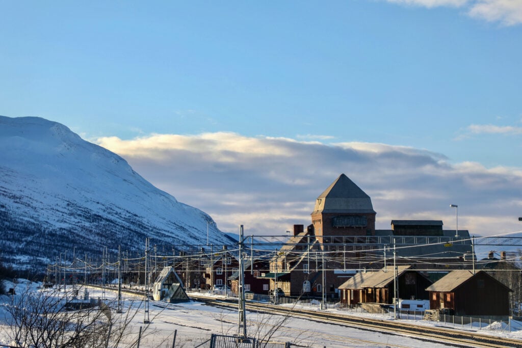En tågstation bredvid ett fjäll, snö ligger på marken.