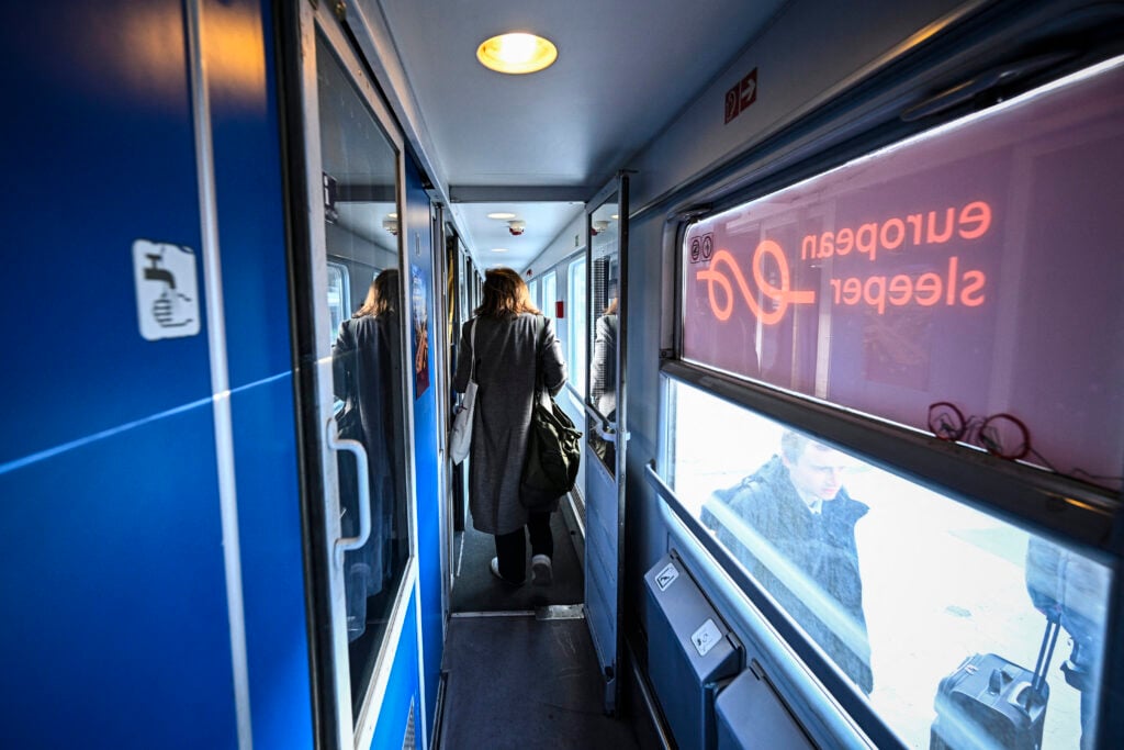 Passagerare går i en tågvagn med blå väggar. European Sleeper står spegelvänt på ett fönster.
