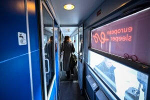 Passagerare går i en tågvagn med blå väggar. European Sleeper står spegelvänt på ett fönster.