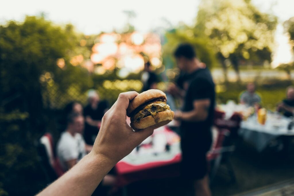 En hand håller i en hamburgare i en park.