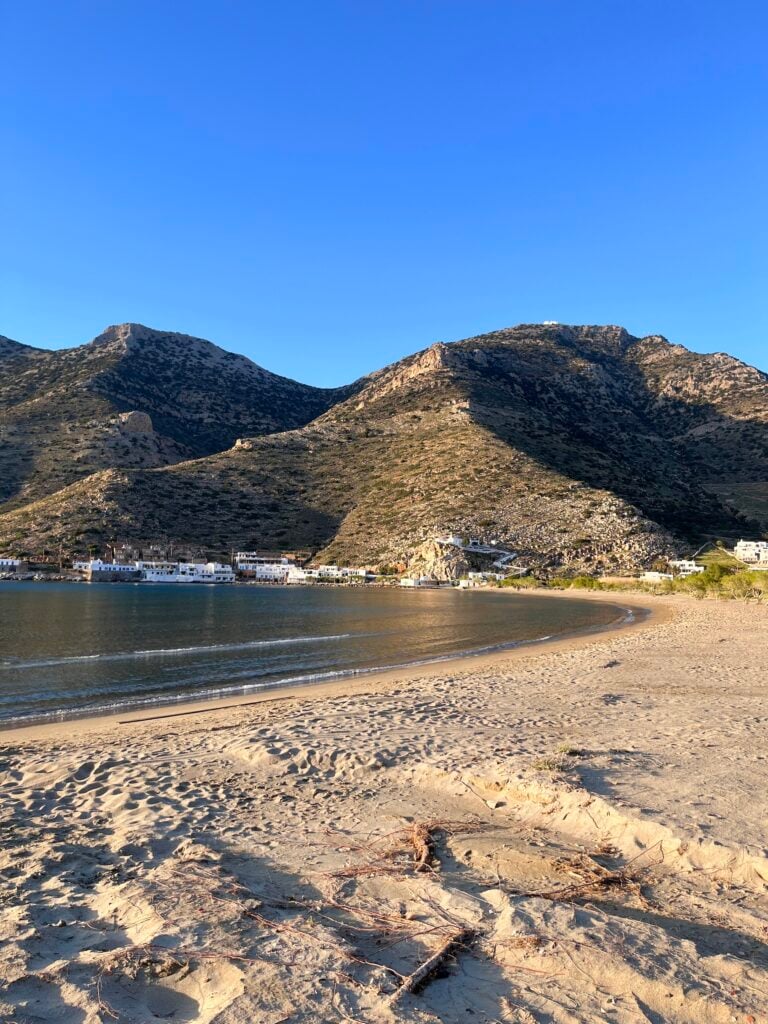 Sandstrand vid lugnt hav, berg i bakgrunden.
