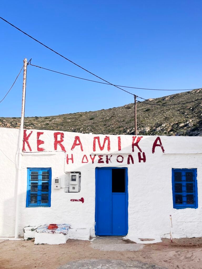 Vitt stenhus med röd grekisk text under blå himmel.