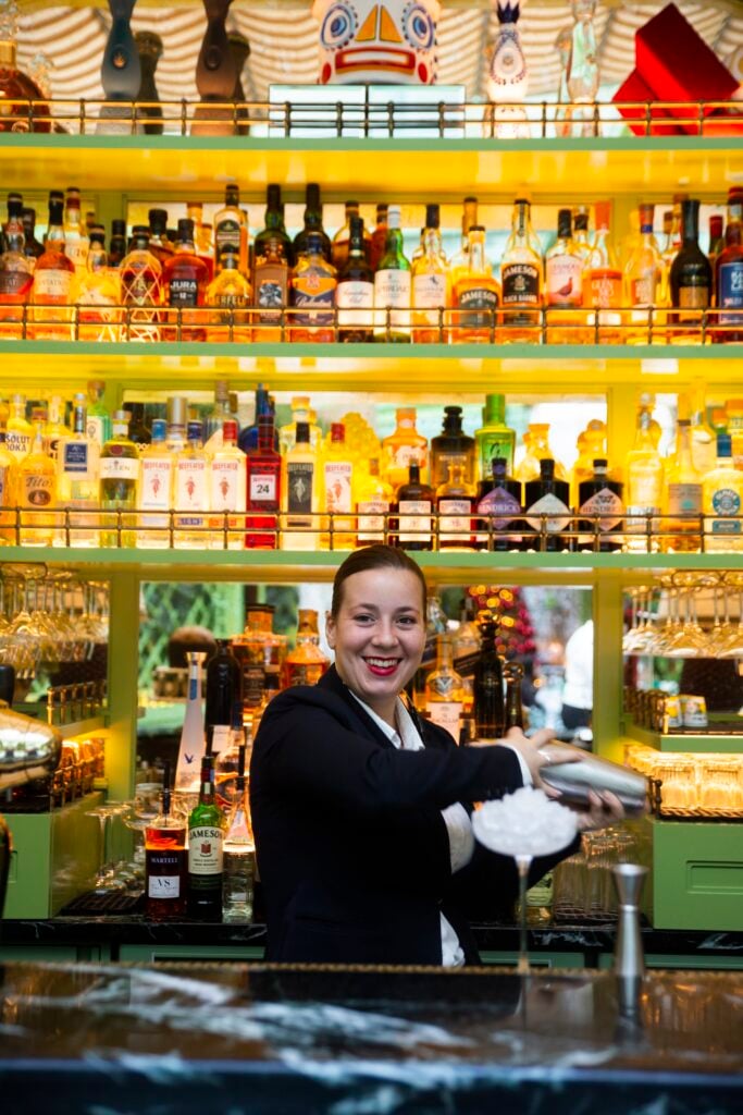 Kvinna i kostym i bar med flaskor i bakgrunden.