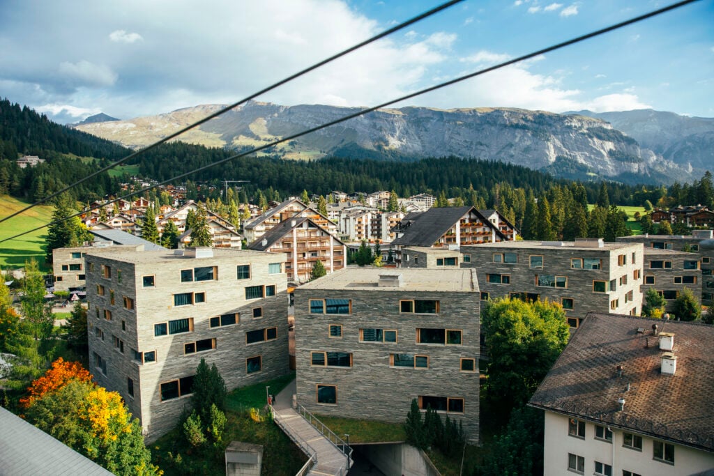 Gråa fyrkantiga tegelbyggnader står längst fram i en alpby.