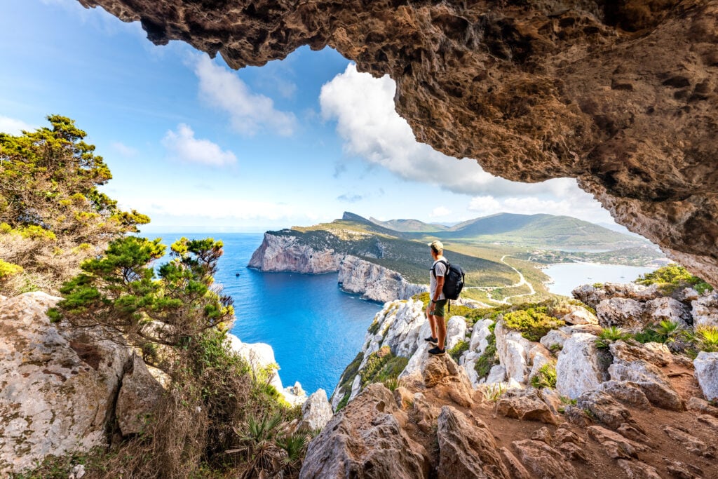 Bergsstig genom en dramatisk bergsklippa, en vandrare tittar på utsikten över havet.