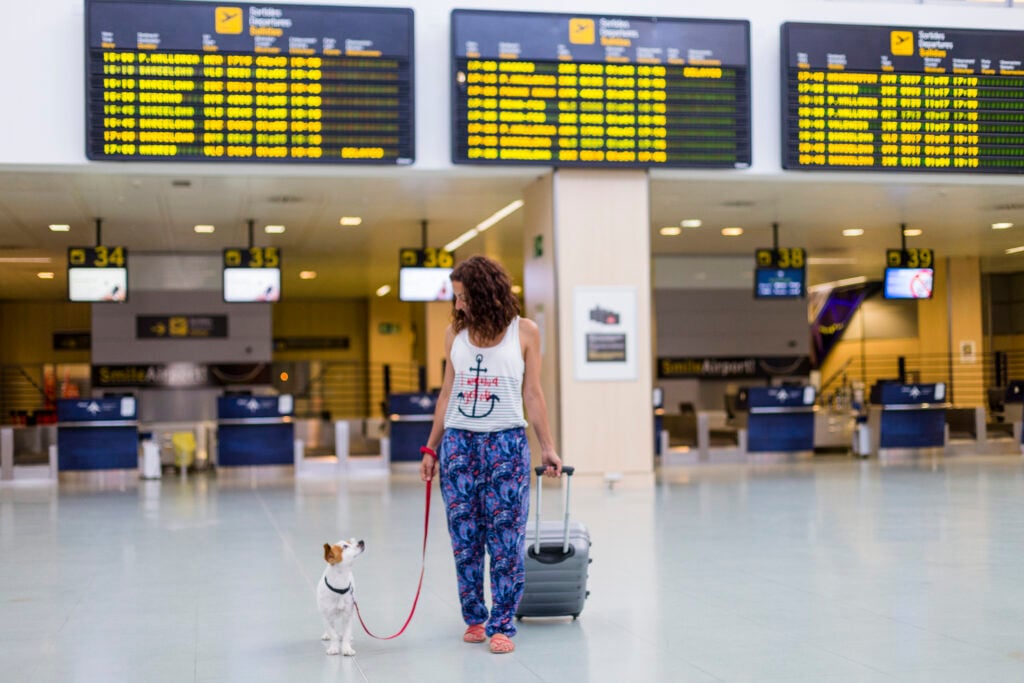 En kvinna håller en hund i ett koppel på en flygplats.