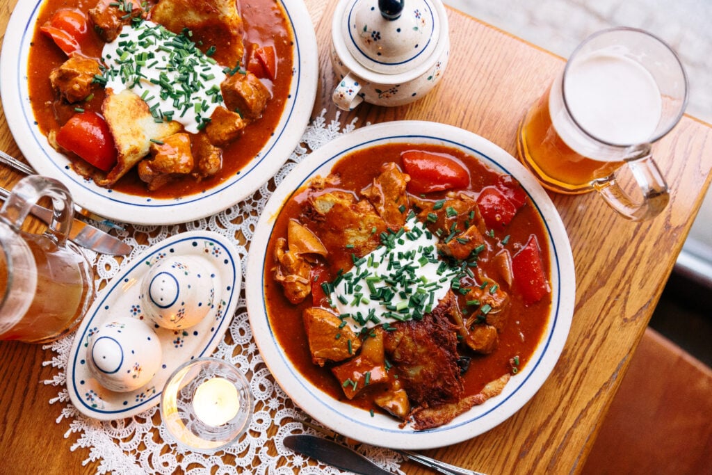 En flatlay med två tallrikar på ett restaurangbord, fylld med någon slags gryta med köttbitar och gräddfil med hackad gräslök.