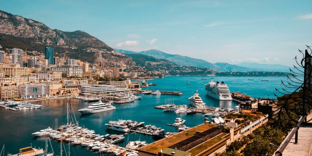 Vacker utsiktsvy över Monaco, vackra lyxiga hus täcker sluttningarna, enorma yachter flyter runt i havet, blå himmel, berg i bakgrunden.