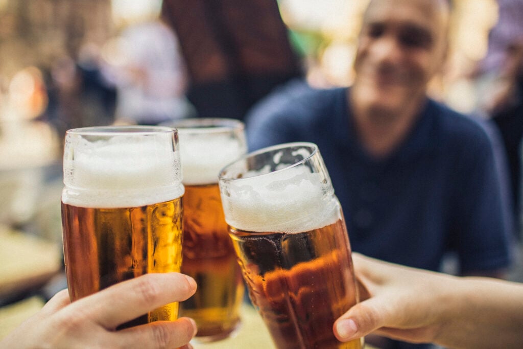 Tre stora ölglas skålas, en person i bakgrunden.