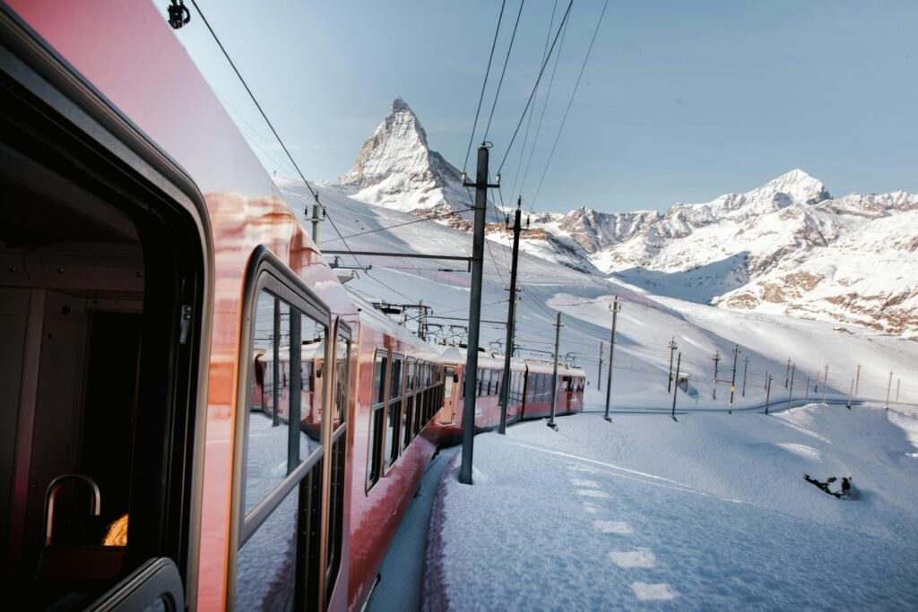 Ett långt rött tåg snirklar sig fram genom Alperna, Matterhorn syns i bakgrunden.