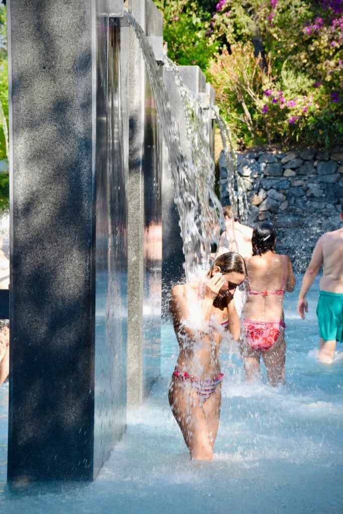 Personer i badkläder duschar bredvid stenar, utomhus i en pool.